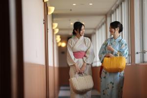 dos mujeres en kimonos parados en un pasillo con cestas en Kyukamura Shikanoshima en Fukuoka