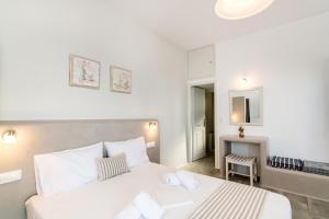 a white bedroom with a large bed and a chair at Porto Bello Tinos in Agios Ioannis