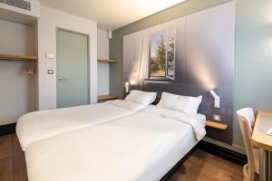 Cama blanca grande en habitación con mesa en B&B HOTEL Dieppe, en Saint-Aubin-sur-Scie