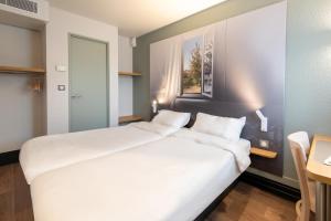 a large white bed in a room with a table at B&B HOTEL Dieppe in Saint-Aubin-sur-Scie