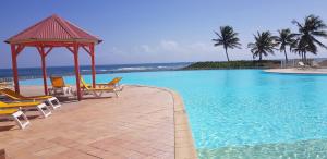 a swimming pool with chairs and a gazebo and the ocean at Le coup de coeur in Saint-François