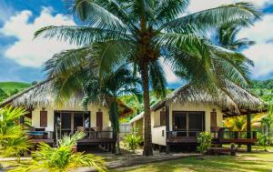 a house with palm trees in front of it at Tamanu Beach in Arutanga