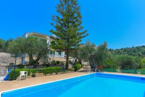 a swimming pool in front of a house with a tree at Fran Apartments in St. Spyridon Corfu