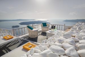 a balcony with chairs and tables and the ocean at Thea Apartments in Imerovigli