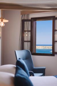 una persona sentada en una silla azul mirando por una ventana en Thea Villas and Suite, en Lindos