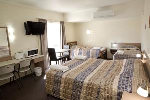 a hotel room with three beds and a desk at Pioneer Motel Goondiwindi in Goondiwindi