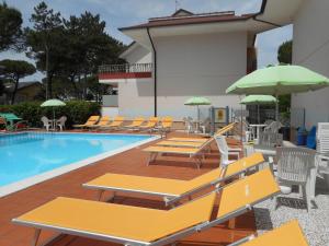 einen Pool mit Stühlen und Sonnenschirmen neben einem Gebäude in der Unterkunft Casa Bianca Village Apartments in Lignano Sabbiadoro