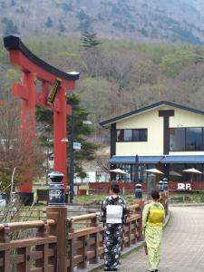 two people walking on a bridge with a building at Okunikko Guesthouse JUN in Nikko