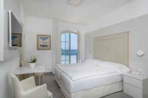 a white bedroom with a bed and a desk and a chair at Hotel Vega in Malcesine