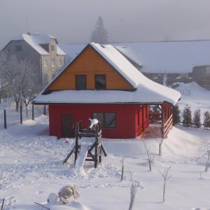 a man standing in front of a red house in the snow at Domek Całoroczny OSTOJA in Istebna