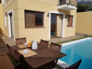 een houten tafel en stoelen naast een zwembad bij Villa Las Salineras in Buenavista del Norte