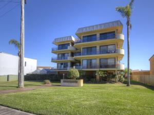 a tall yellow building with palm trees in front of it at Champagne Court 1 in Tuncurry