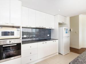 a white kitchen with white cabinets and a microwave at Regatta 13 in Forster