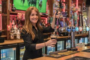 a woman standing behind a bar holding a drink at Central Station Hotel Liverpool in Liverpool