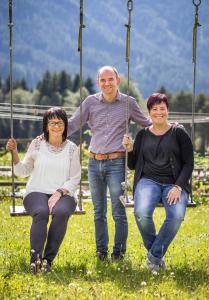 a man and two women sitting on a swing at Klein Fein Hotel zum Graf in Valle Di Casies