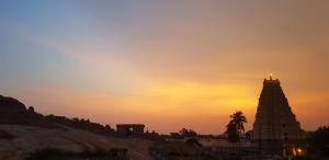 a sunset with a building and a palm tree at Padmaa Hampi Villa in Hampi