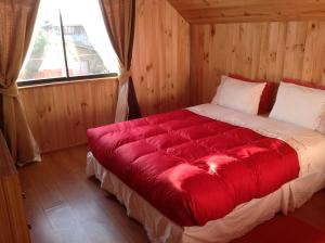 Cama roja en habitación con ventana en Hostal Monica, en Pucón