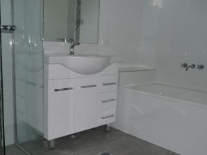 a white bathroom with a sink and a bath tub at The Breakers 13 in Forster