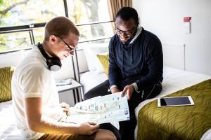 deux hommes assis sur un lit en train de regarder une carte dans l'établissement YMCA Hostel, à Auckland