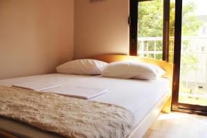 Mimoza Apartments في دينوفيتسي: سرير بملاءات ومخدات بيضاء بجانب نافذة