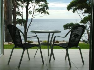 two chairs and a table on a porch with the ocean at Mollymook Beach Waterfront in Mollymook