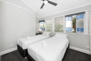 Beautiful Queenslander في تاونزفيل: سريرين في غرفة بجدران بيضاء ونوافذ