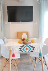 mesa de comedor con sillas blancas y TV de pantalla plana en Cornelia Apartment, en Palaión Tsiflíkion