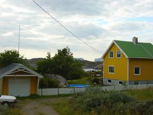 a yellow house with a green roof next to a fence at Edvinstua in Pettvik