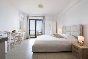 a white bedroom with a large bed and a kitchen at Kimata Apartments in Arkasa