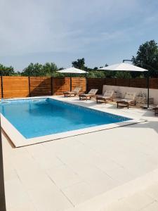 a swimming pool with chairs and umbrellas on a patio at Apartments Malic in Pridraga