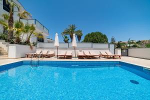 una piscina con sillas y sombrillas junto a un edificio en Baldacchino Holiday Villas, en Mellieħa