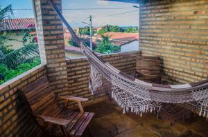 a hammock on a balcony with a chair and a window at Pousada Morada do Sol in Canoa Quebrada