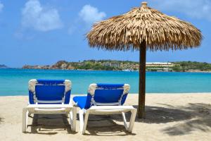 two chairs under a straw umbrella on the beach at Emerald Beach Resort in Lindbergh Bay