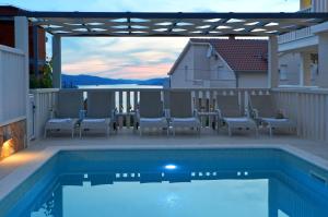 a swimming pool with chairs and a pergola on a patio at Apartments Tomislav in Trogir