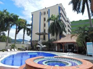 a swimming pool in front of a building with palm trees at Hotel Maria Gloria in Villavicencio