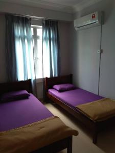 two beds in a room with purple sheets and a window at PD Homestay Laguna / Ocean Apartment in Port Dickson