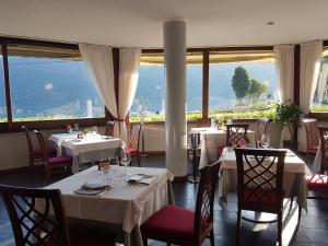 un restaurante con mesas y sillas blancas y ventanas en Hotel & Residence La Sibilla Cusiana en Pettenasco