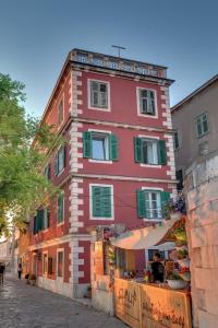 a red building with green shutters on a street at Apartment Oliveto Sibenik in Šibenik
