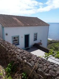 una casa blanca con una pared de piedra junto al océano en Casa da Matilde, en Fajã de São João