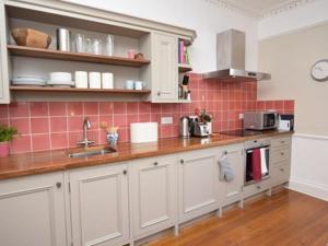 a kitchen with white cabinets and pink tiles at Burton House Apartment in Lyme Regis