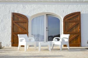 3 chaises blanches assises devant une porte dans l'établissement Hotel Rural Binigaus Vell, à Es Migjorn Gran
