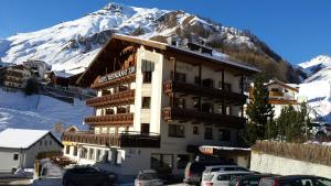 a building with cars parked in front of a mountain at Hotel Edi in Samnaun