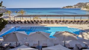 una piscina con sombrillas y sillas y la playa en Secrets Mallorca Villamil Resort & Spa - Adults Only (+18), en Paguera