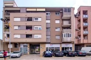 een hoog gebouw met auto's geparkeerd op een parkeerplaats bij Grove Apartment + Free Parking in Novi Sad