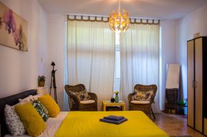 a bedroom with a yellow bed and chairs and a chandelier at Collosal Studio in Bucharest