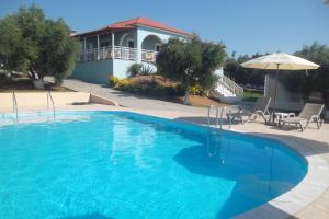 a large blue swimming pool with an umbrella and a house at Kastro Beach Hotel in Kyllini