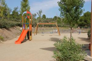 un parque infantil vacío con un tobogán naranja y un columpio en Càmping Terra Alta, en Bot