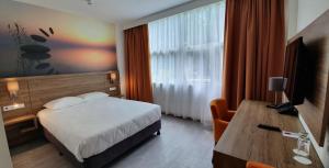 Habitación de hotel con cama, escritorio y TV. en Atlas Hotel Holiday en Spijkenisse