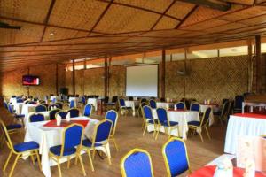 Habitación grande con mesas, sillas y una pantalla. en Fort Breeze Hotel, en Fort Portal