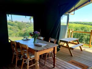 a wooden table and chairs on a deck with a view at Brackenhill Glamping - Safari Tent with Hot Tub in Ivybridge